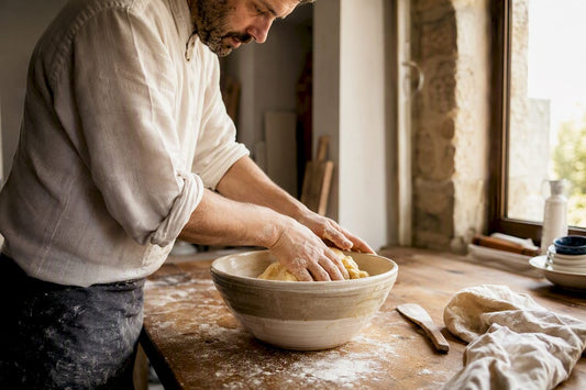 Un boulanger façonne délicatement la pâte à brioche dans son saladier, en la repliant pour lui donner sa texture aérienne.